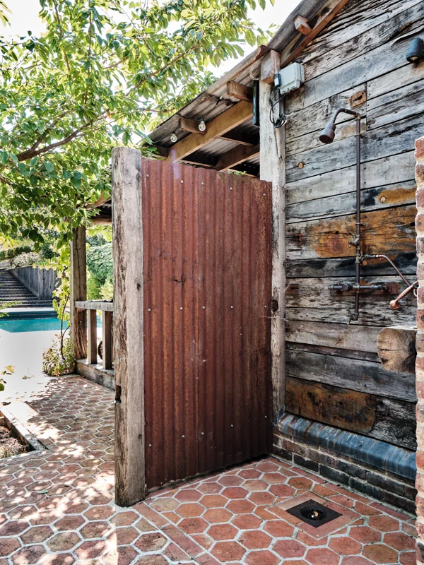 Weathered timber garden building with brick paving and a red door